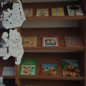 Otwórz zdjęcie - Książki o Kubusiu Puchatku leżące na półkach regału w bibliotece.